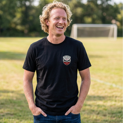 Man on a football pitch wearing a black t-shirt with the Two Footed Tackle FC crest on the left chest