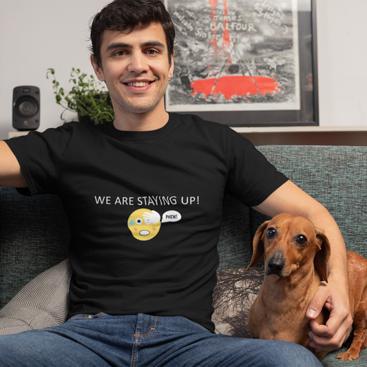 Man wearing a black t-shirt with text  of we are staying up with a emoji that shows the phew sign and a dog sitting on a couch in a living room.