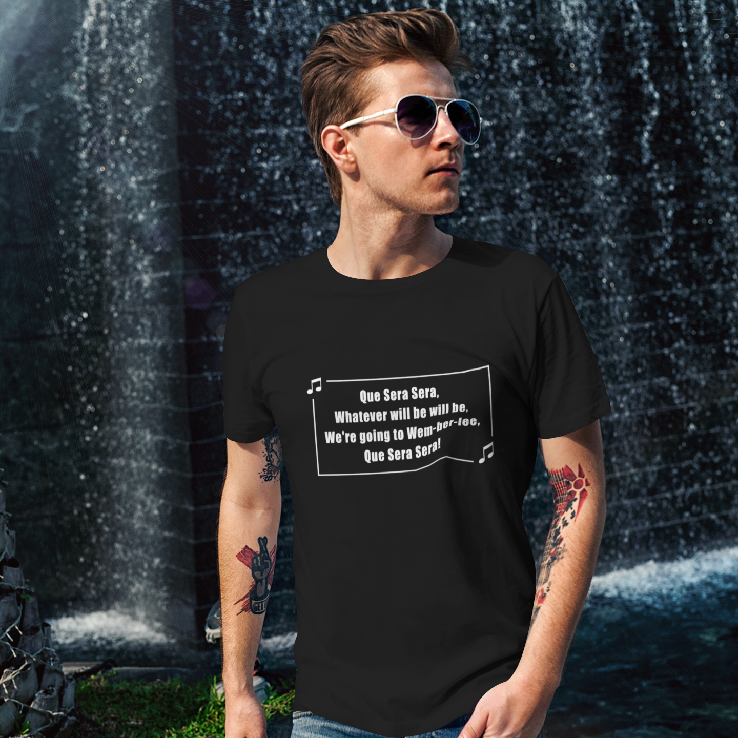 Man wearing a black t-shirt with a graphic design of a football song que Sera Sera, we're going to Wembley in front of a water fountain